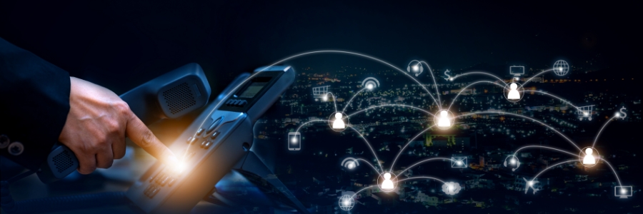 Hand holding a VoIP desk phone with glowing network connection icons over a city skyline at night