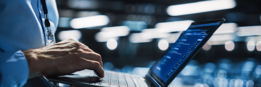 IT technician typing on laptop displaying blue code interface in a dark server room environment