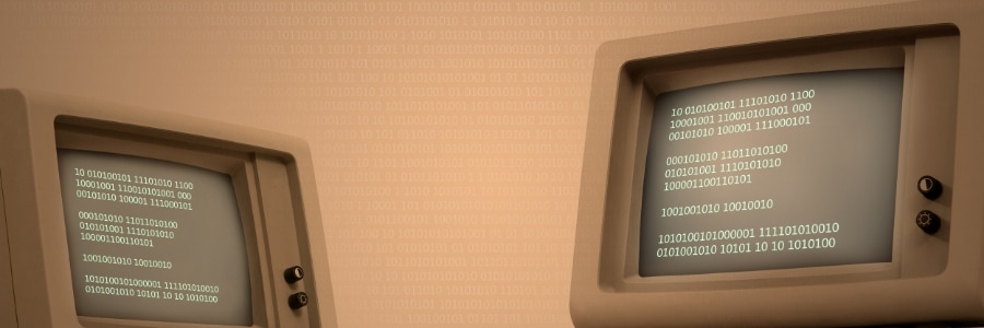 Two vintage computer terminals displaying binary code on green-tinted screens, representing legacy IT systems