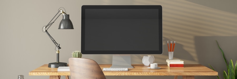 Clean wooden desk with desktop PC monitor, keyboard, lamp, and office supplies in a modern home workspace