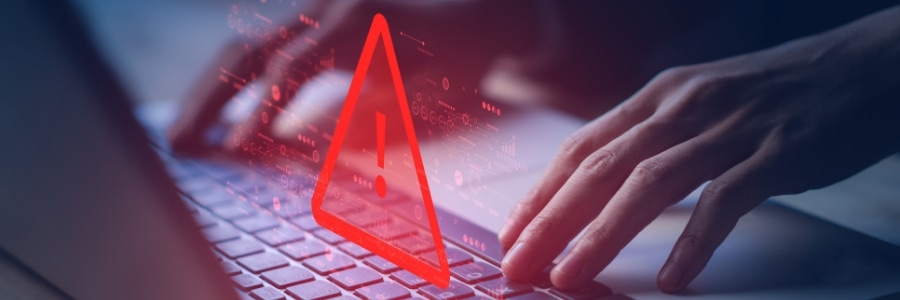 Hands typing on laptop keyboard with red warning triangle alert symbol and digital data overlay