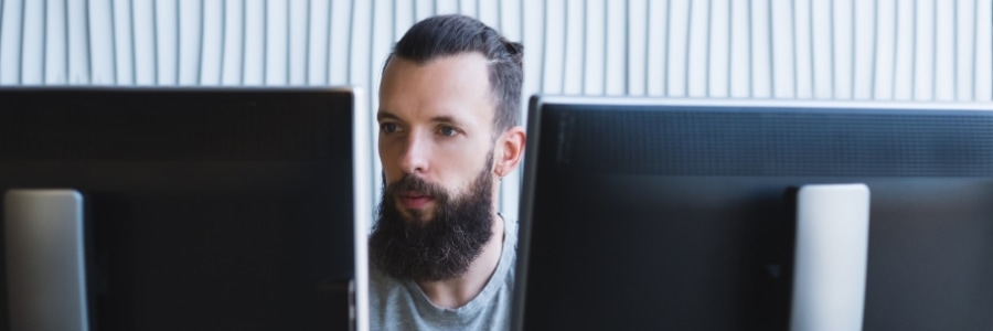 IT professional working at dual monitor computer setup in modern office workspace