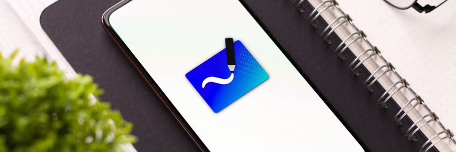 Microsoft Whiteboard app icon displayed on a smartphone screen beside a spiral notebook and plant
