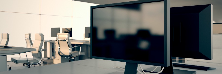 Modern office workstation with dual computer monitors on a desk, additional workstations and chairs visible in background