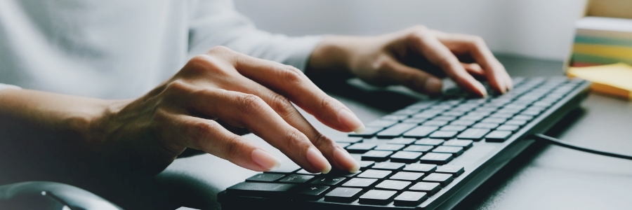 Hands typing on a black wired keyboard at a desk, representing productivity and Windows computer usage