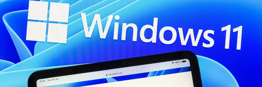Windows 11 logo and branding displayed on a blue screen alongside a tablet showing the Microsoft website