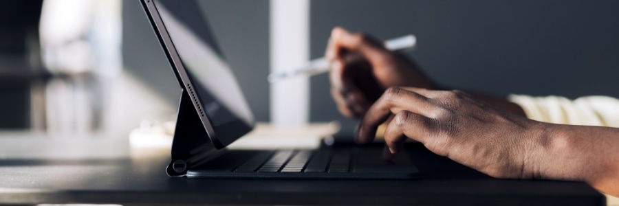 Hands typing on a tablet keyboard while holding a stylus, working on a small business computer setup