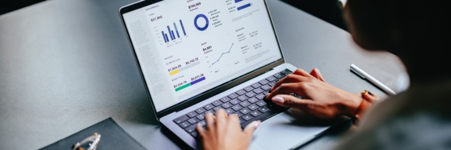 Person typing on laptop displaying business dashboard with charts, graphs, and financial data metrics