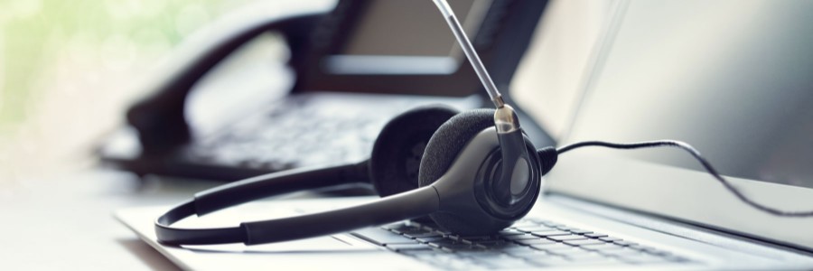 Wired headset with microphone resting on laptop keyboard beside a desk phone for business VoIP communication