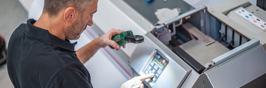 IT technician inspecting industrial machine control panel with handheld scanner in manufacturing facility