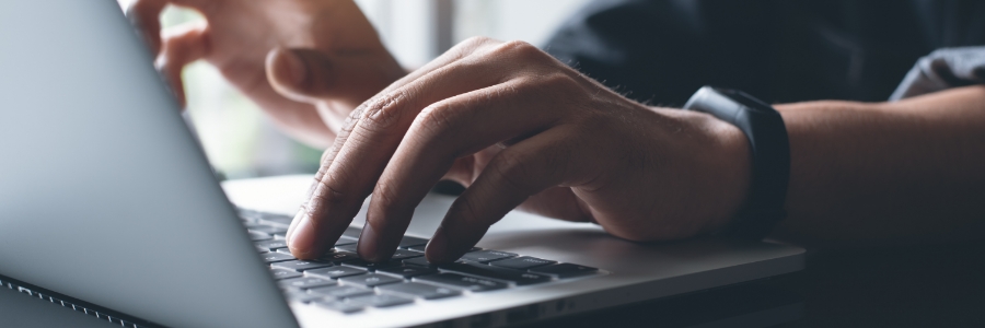 Person typing on laptop keyboard while wearing a smartwatch, close-up view of hands on computer for remote work