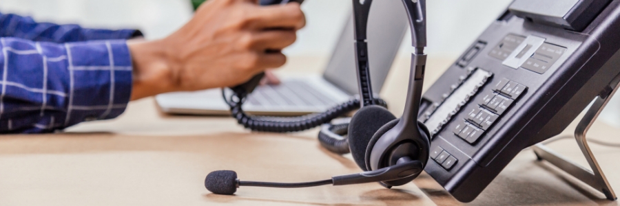 VoIP desk phone and headset on office desk with person using handset in background