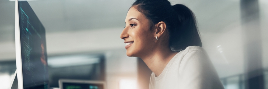 Smiling professional woman reviewing cloud-based data on computer monitors in a modern IT office environment