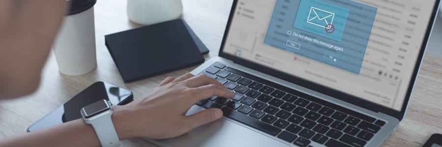 Person typing on laptop displaying email notification popup, with smartwatch and phone on desk nearby