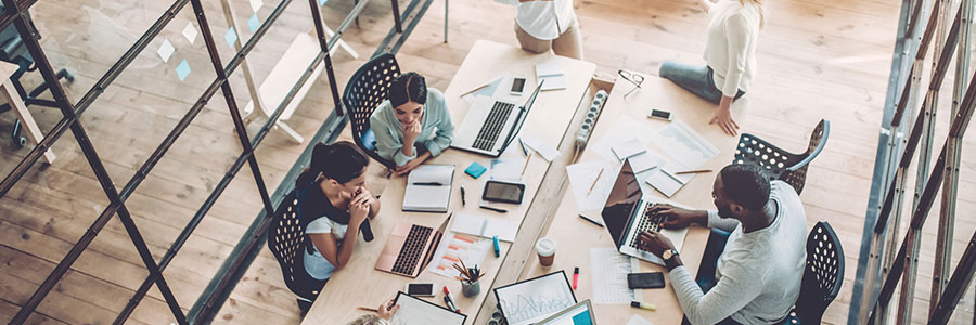 Diverse team of employees collaborating around a conference table with laptops and documents in a modern office