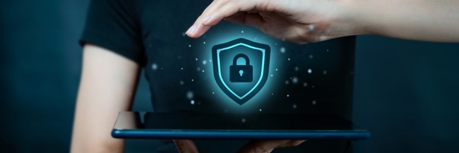 Person holding tablet with glowing cybersecurity shield and padlock icon floating above, representing digital protection