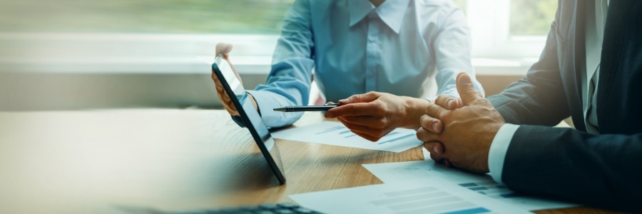 Two business professionals reviewing IT documents and data charts at a desk with a tablet during a consultation meeting