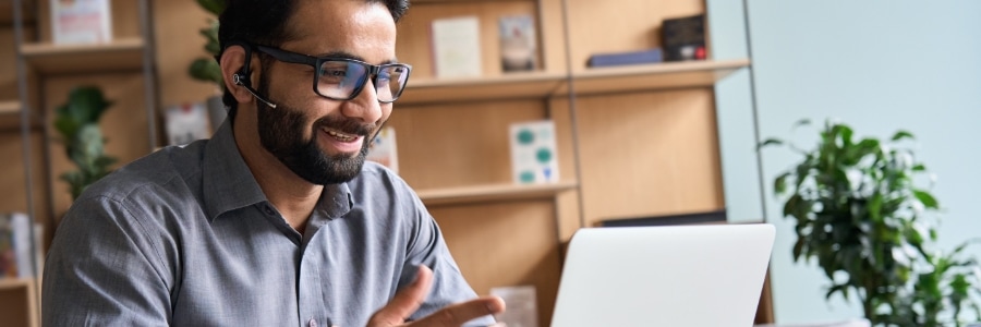 Man with bluetooth headset speaking on video call via laptop in modern office workspace