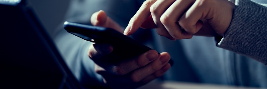 Two hands using a smartphone in low light, troubleshooting slow mobile internet connectivity