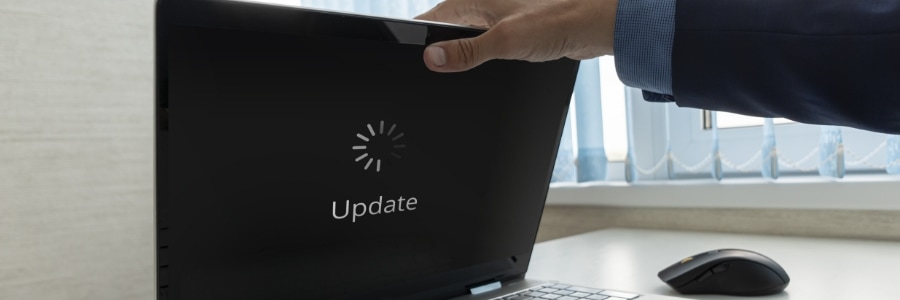Person opening a black laptop displaying a loading spinner and Update text on the lid, mouse on desk nearby