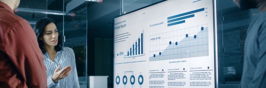 Business professional presenting annual report data on large office display screen with charts and graphs