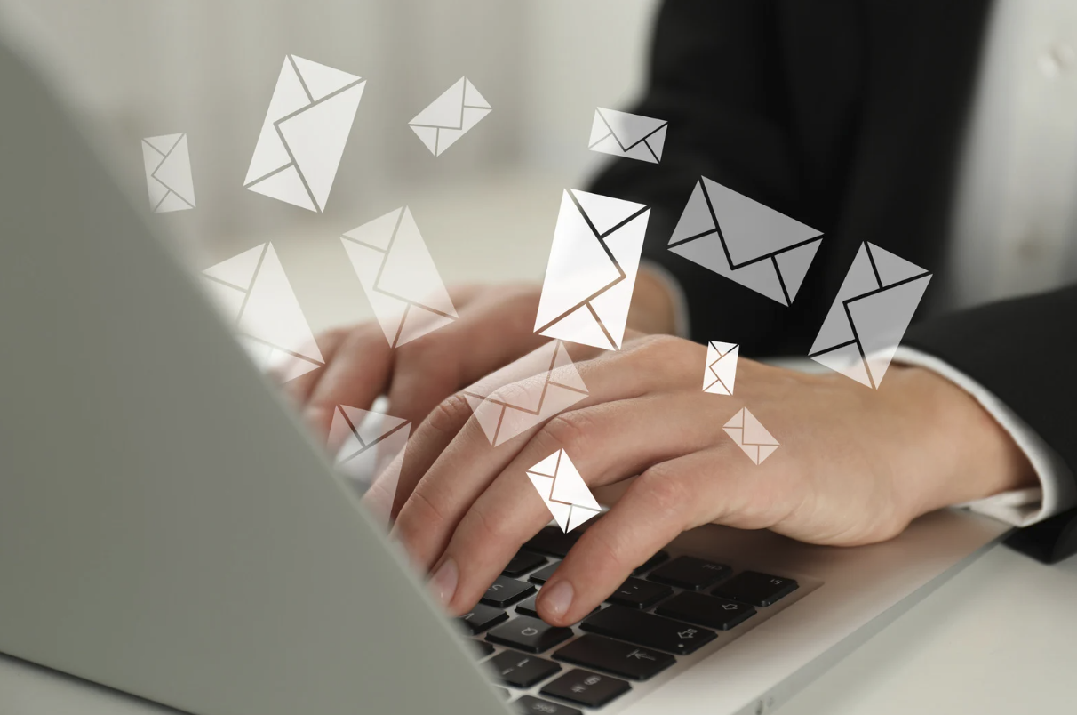 Business professional typing on laptop with digital email envelope icons floating above the keyboard