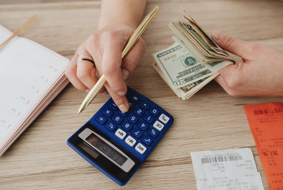 Hands using calculator and counting cash next to receipts and notebook for financial IT services budgeting
