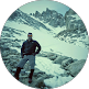 Man standing confidently on rocky mountain terrain with snow-covered peaks in background