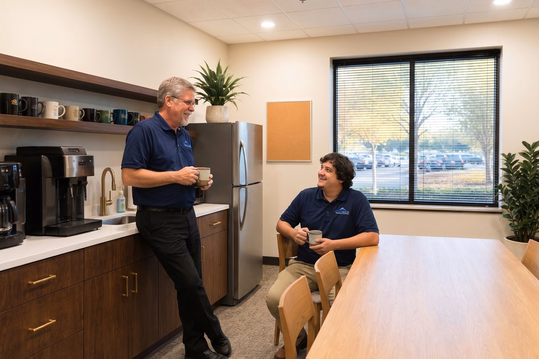 Two IT professionals sharing coffee and collaborating in a modern office break room, representing co-managed IT partnership