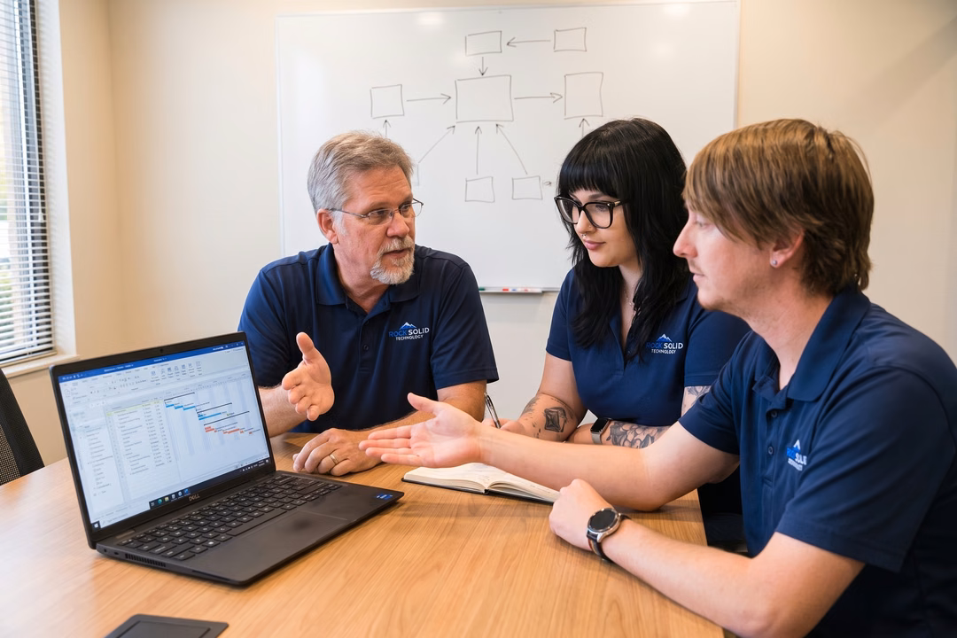 Rock Solid Technology IT team reviewing project management software on a Dell laptop during a conference room meeting