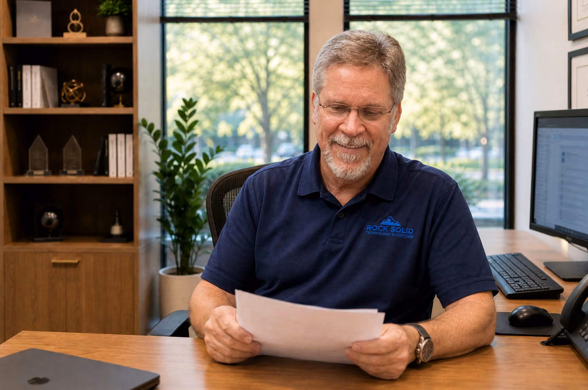 Rock Solid Technology Solutions IT professional reviewing cybersecurity documents at office desk with computer