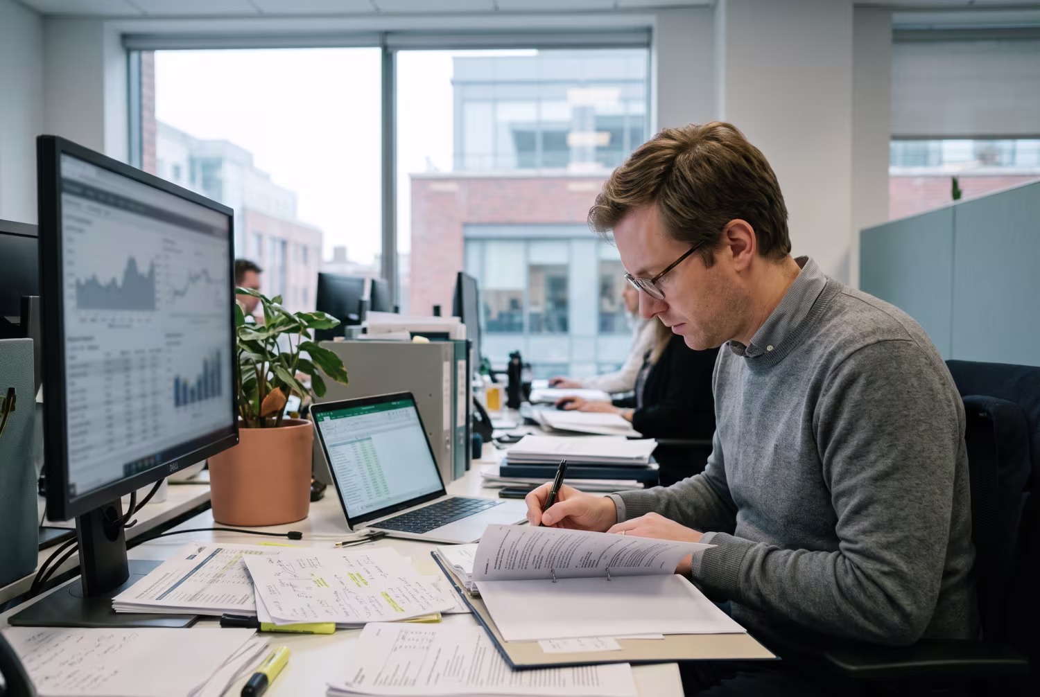 Finance professional analyzing reports at desk with sunlight and QuickBooks cloud hosting on monitor