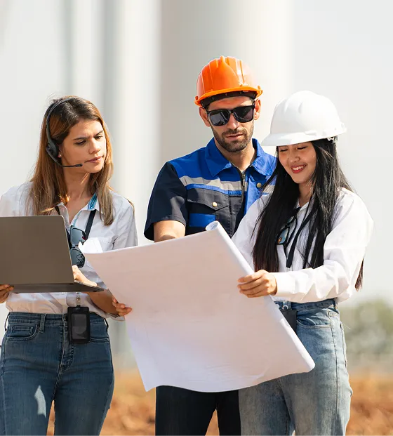 Two engineers in hard hats and a woman with headset review blueprints and a laptop outdoors.