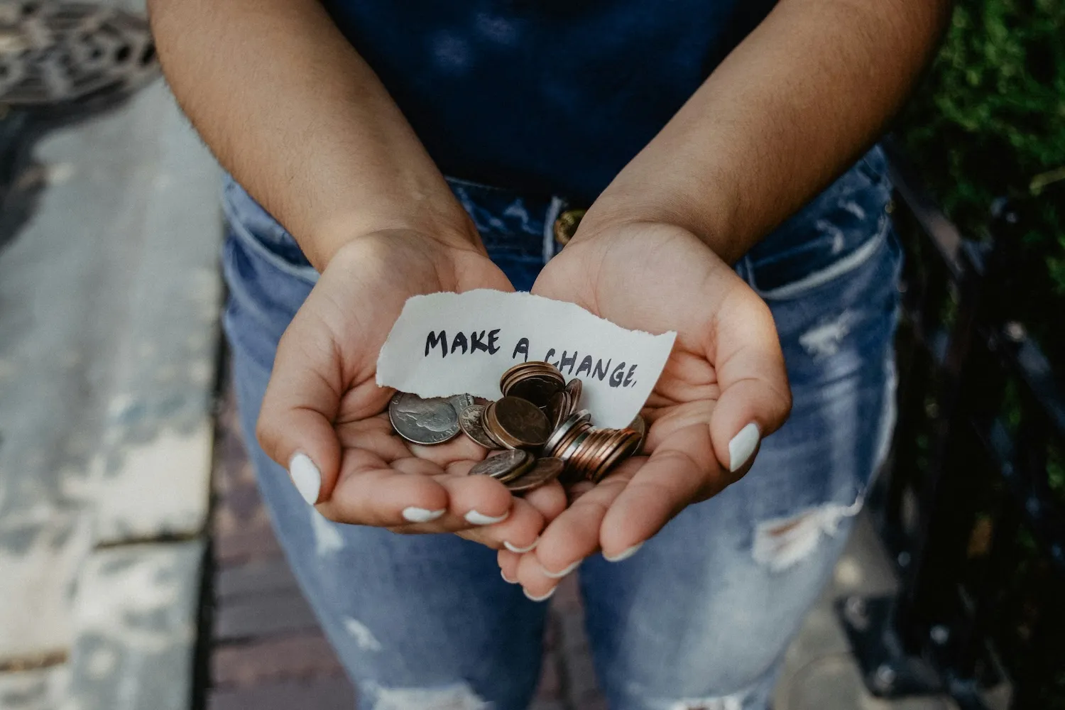 Hands holding coins and a torn paper note reading 'MAKE A CHANGE'.