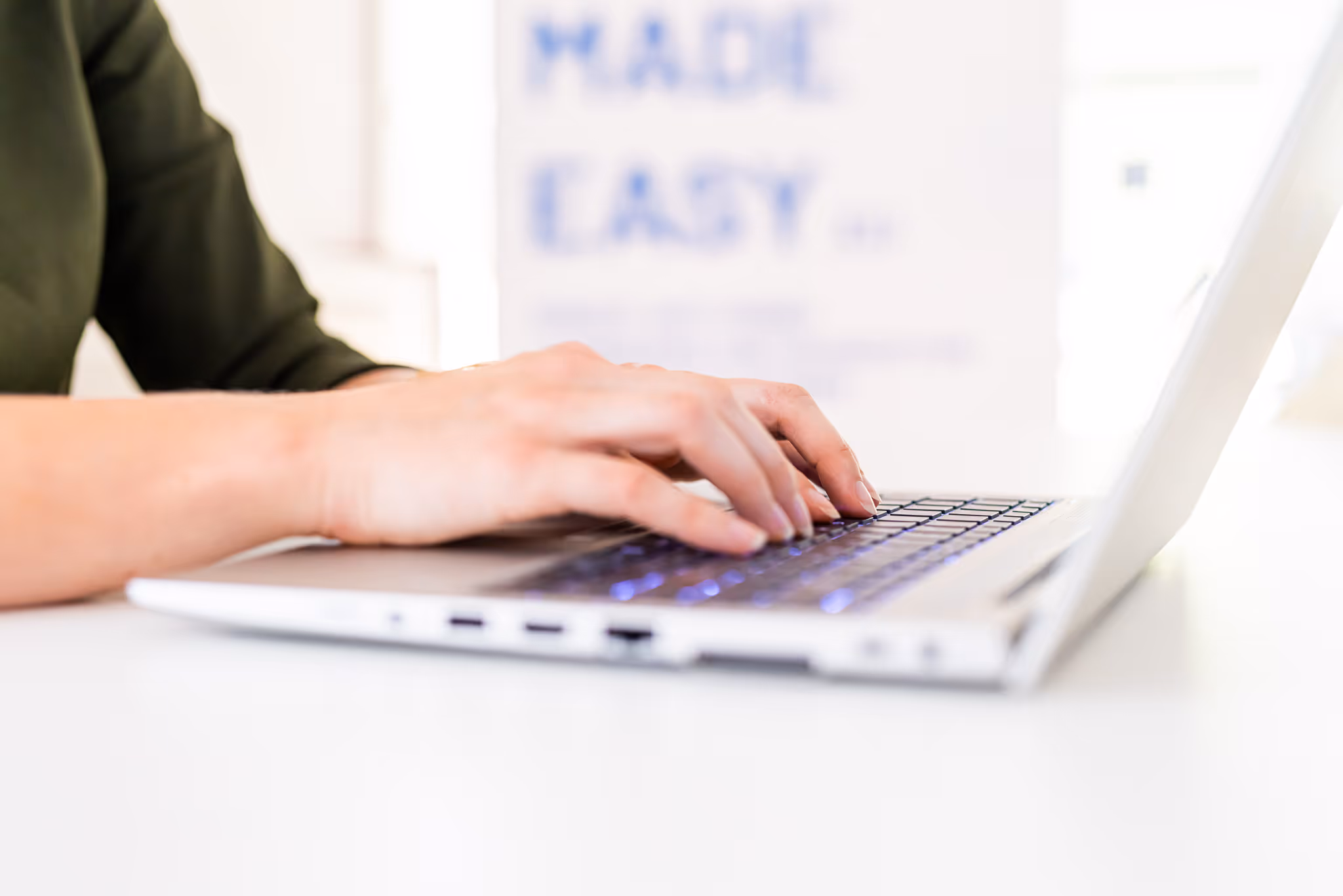 Handen typen op een laptoptoetsenbord met een wazige tekst op de achtergrond.