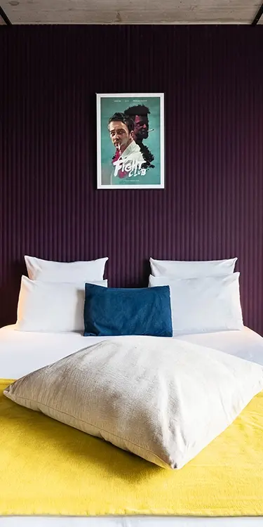 Recadrage vertical resserré sur le lit à couverture jaune et coussins bleu marine, sous l'affiche du film Fight Club
