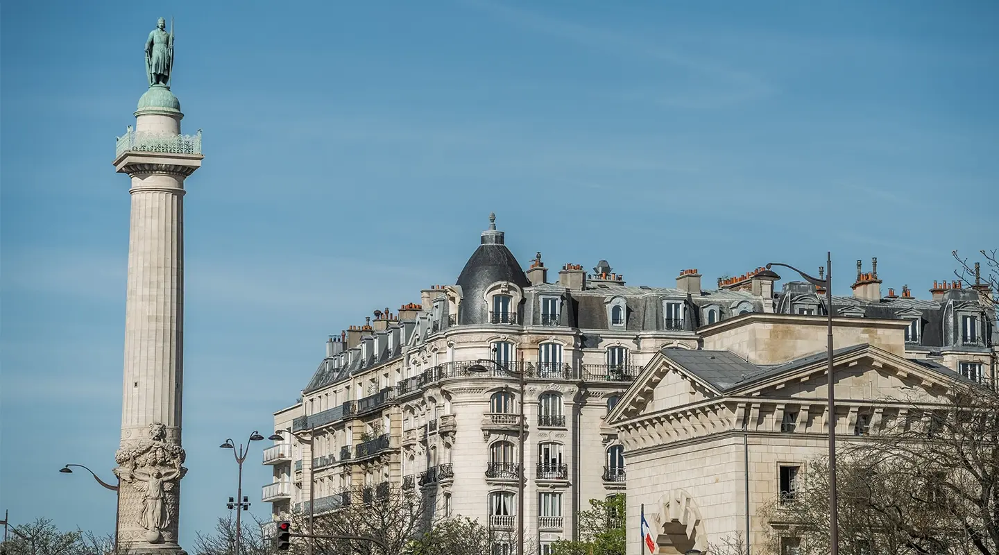 Vue en format portrait de la colonne de la place de la Nation avec sa statue en bronze, immeuble parisien à balcons en arrière-plan