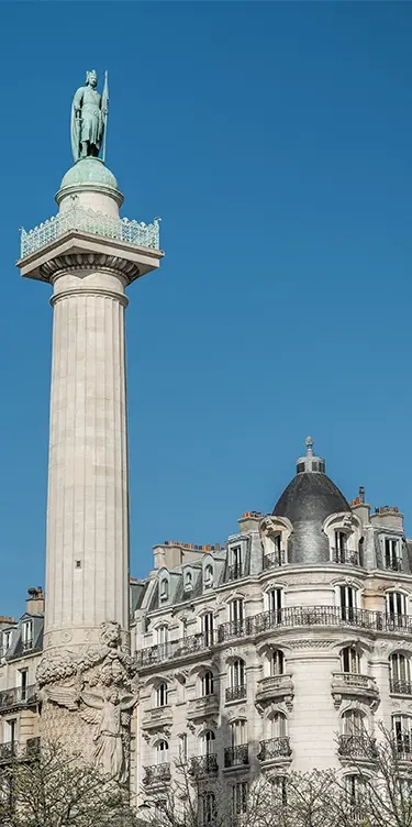 Vue en format portrait de la colonne de la place de la Nation avec sa statue en bronze, immeuble parisien à balcons en arrière-plan