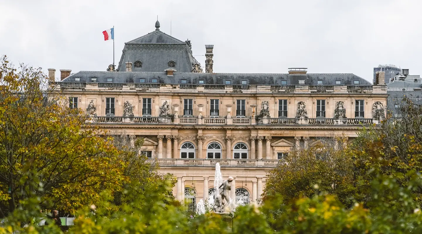 The classic façade of the Palais Royal with the French flag, surrounded by autumnal trees and a fountain in the foreground