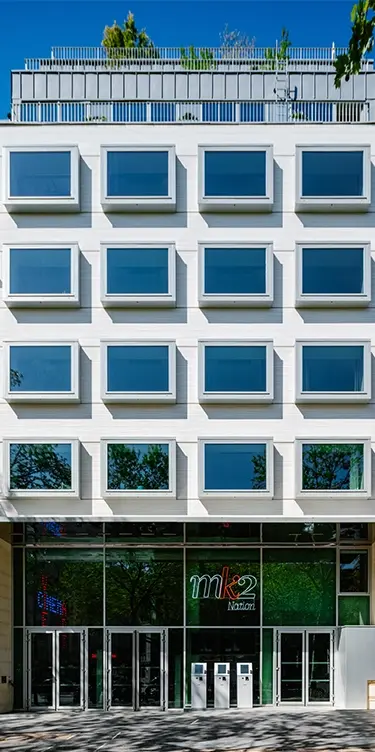 Façade blanche moderne à fenêtres alignées avec toit-terrasse végétalisé, entrée du cinéma mk2 Nation au rez-de-chaussée