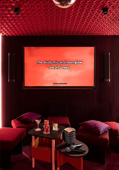 Red karaoke lounge with tufted banquettes, a disco ball, and a screen displaying song lyrics