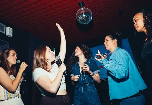 A group of friends partying, dancing, and singing karaoke under a disco ball.