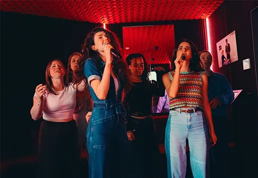 A group of friends singing passionately in a karaoke room with red ambient lighting.