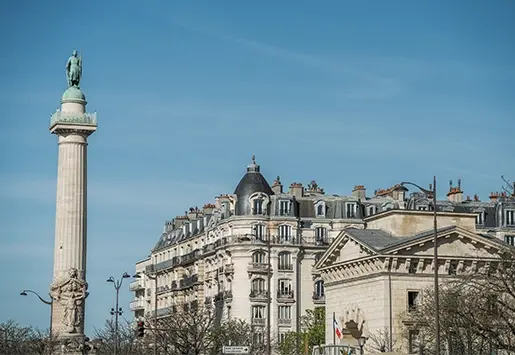 Colonne de la place de la Nation surplombant les toits parisiens, immeuble à dôme et façade classique en arrière-plan
