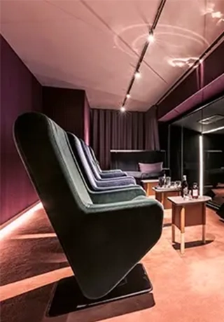 Salle de projection privée aux tons violines avec rangée de fauteuils en velours et petites tables basses.