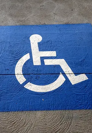 Pictogramme blanc d'accessibilité handicapé peint sur fond bleu sur le sol d'un parking.