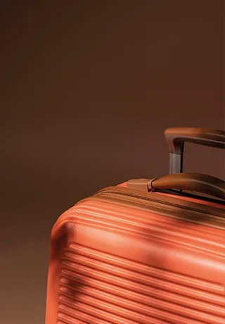 Gros plan sur une valise rigide de couleur terracotta avec poignée en cuir marron.