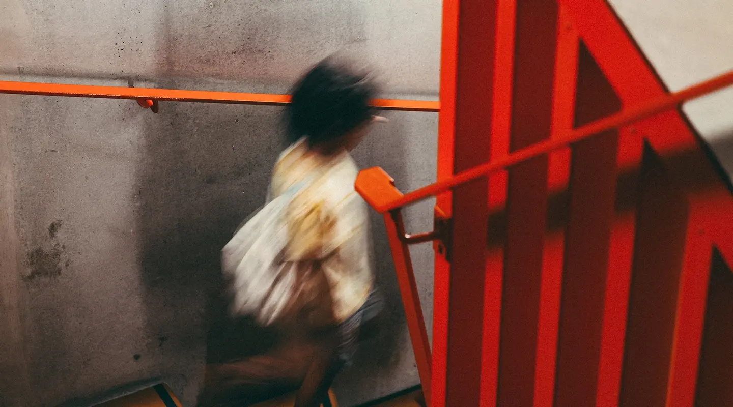 Person walking down a spiral staircase with orange steps and railings, beneath a poster for the film City Lights