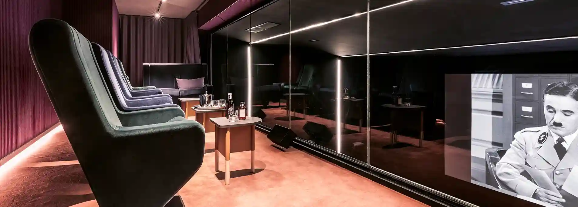 Salle de cinéma privée aux fauteuils vert sapin alignés, murs miroirs noirs et écran projetant une scène de film en noir et blanc