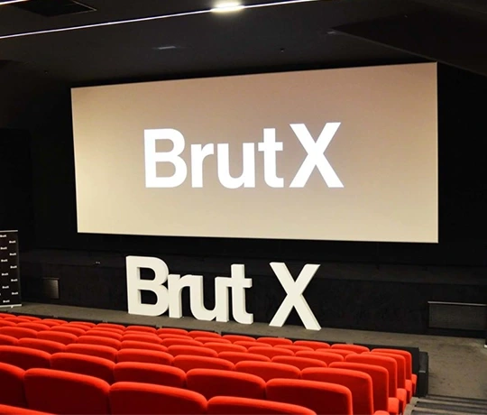 Movie theater with red seats set up for a BrutX event, featuring the logo displayed on the big screen and in giant letters on the stage.